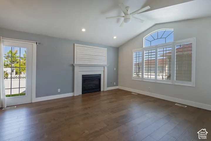 Vaulted ceiling with a ceiling fan, wood-finish flooring, recessed lighting, and a fireplace featuring a white mantel and shiplap-style accent wall