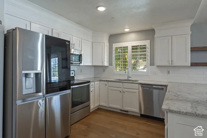 White shaker cabinetry, stainless steel appliances, white subway tile backsplash, granite countertops, and wood-finish flooring