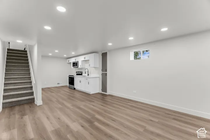 Spacious room featuring wood-finish flooring, recessed lighting, and a built-in kitchenette with white cabinetry and stainless steel appliances