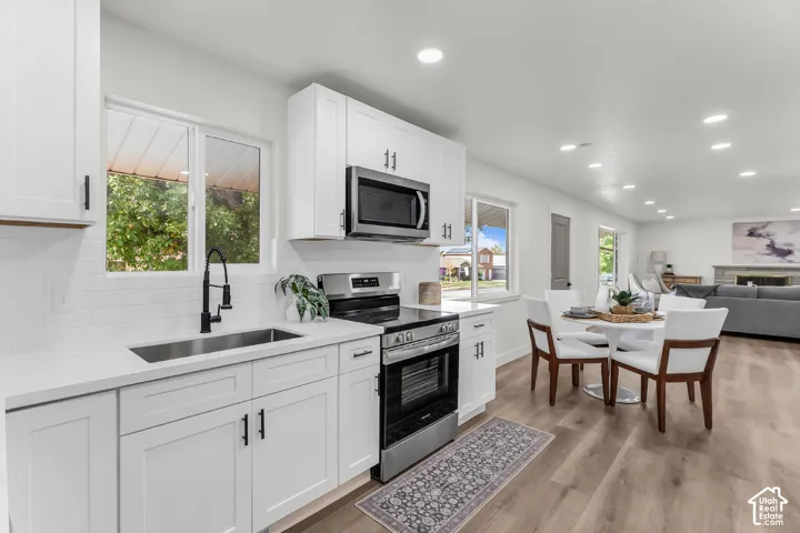 Kitchen featuring white shaker cabinetry, stainless steel appliances, white subway tile backsplash, and wood-finish flooring