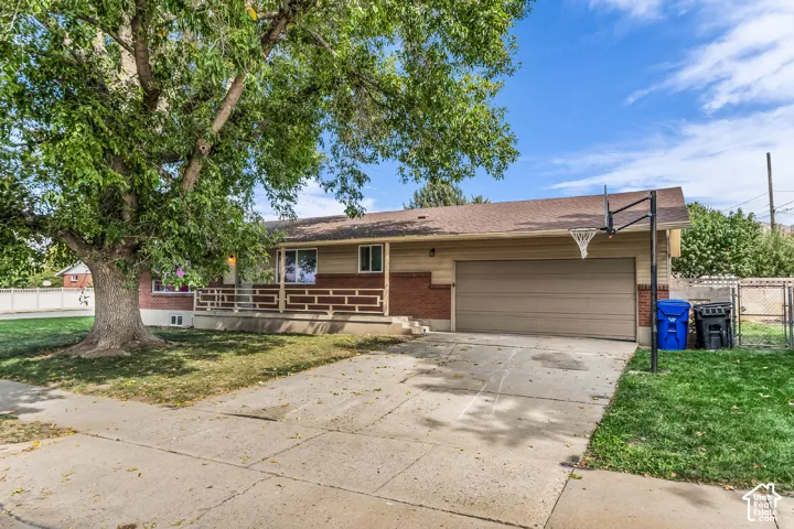 Brick and siding exterior with covered porch, mature front yard tree, attached garage, and paved driveway