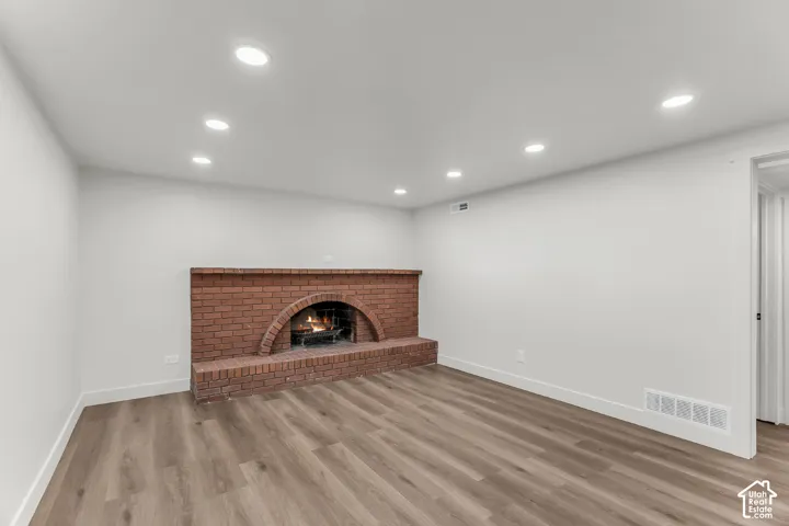Brick fireplace with arched firebox, wood-finish flooring, recessed lighting, and white walls