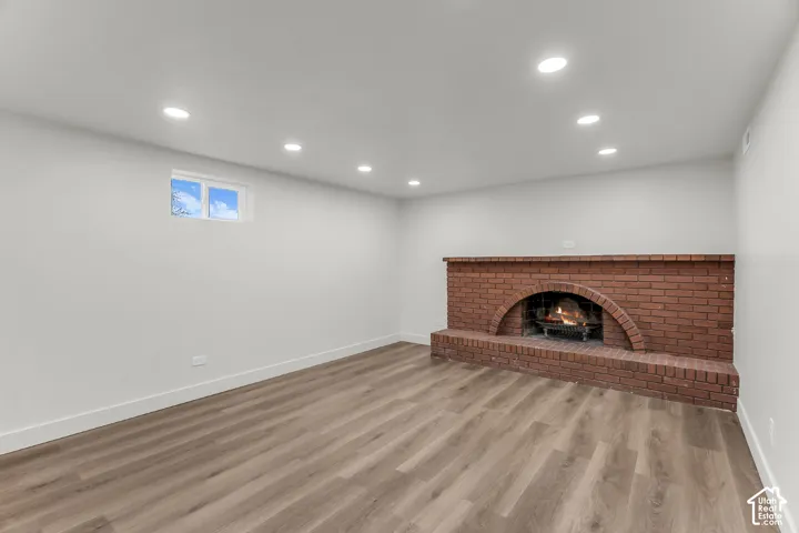 Recessed lighting, wood-finish flooring, and a brick fireplace with an arched firebox