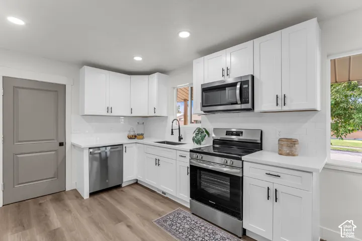 White cabinetry with matte black hardware, stainless steel appliances, white subway tile backsplash, light wood-finish flooring, and solid surface countertops