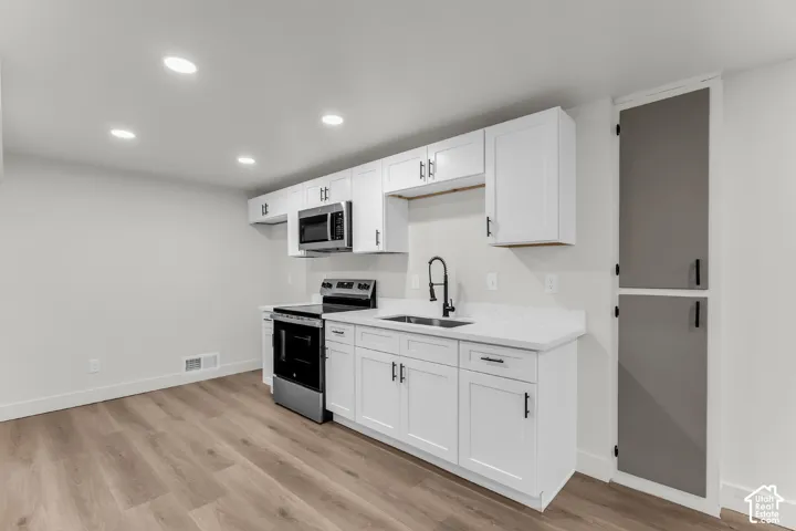 Kitchenette featuring white cabinetry, a stainless steel range, a stainless steel microwave, a black faucet, and wood-finish flooring