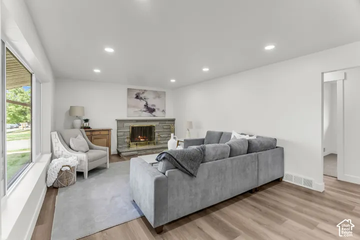 Recessed lighting, wood-finish flooring, stone-clad fireplace, large window, and white walls