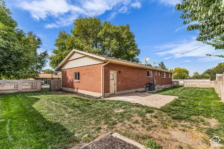 Expansive backyard featuring a brick exterior, concrete patio, mature trees, and decorative block fencing