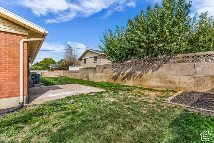 Brick exterior with a rain gutter system, concrete patio area, and a tiered concrete block fence