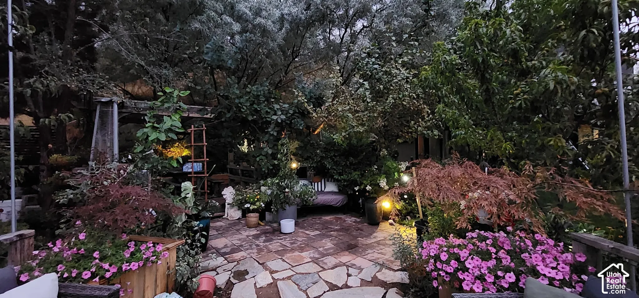 Expansive outdoor living area featuring a stone patio, mature trees, and planted foliage