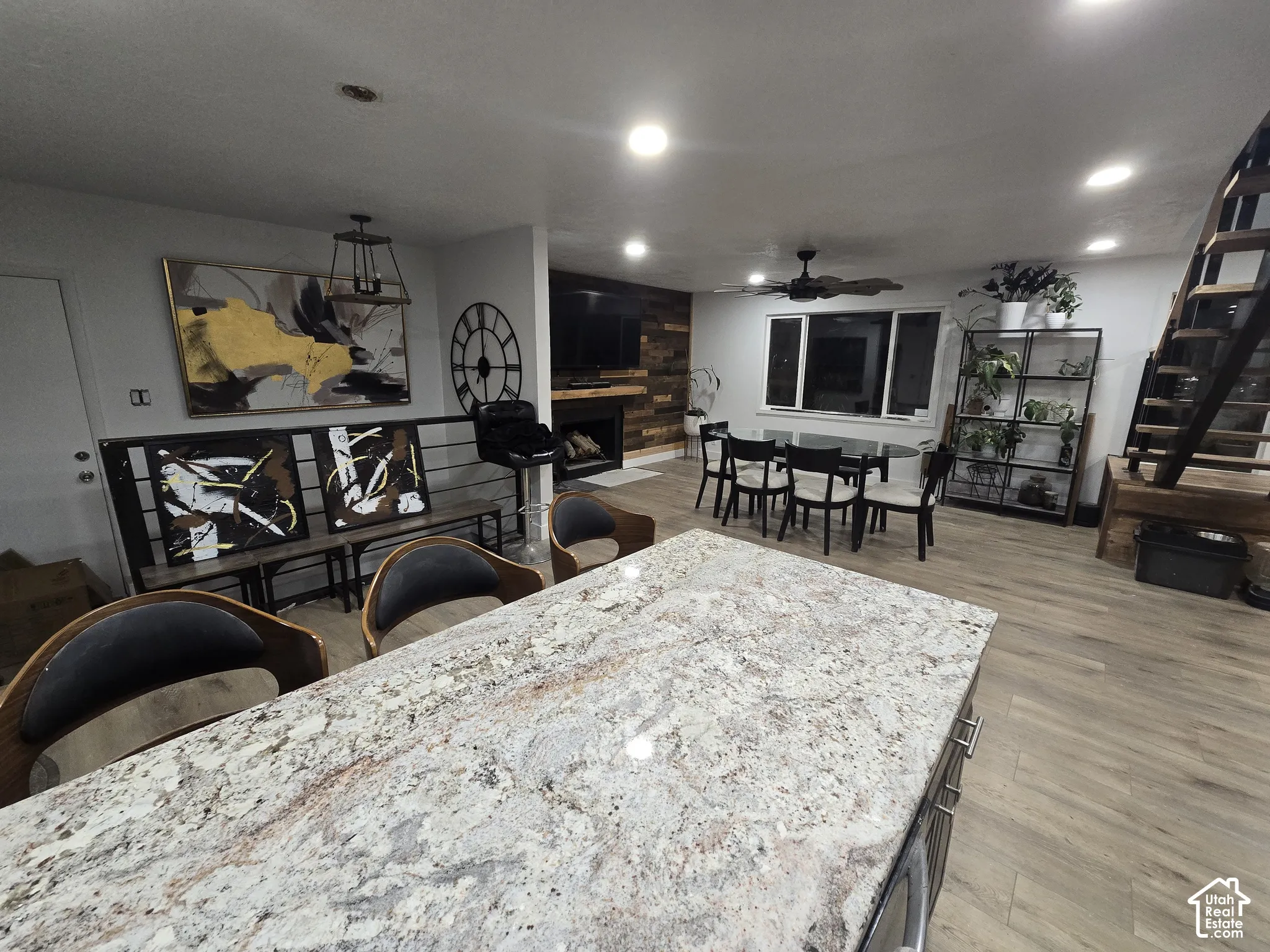 Integrated living space featuring wood-finish flooring, a built-in fireplace with wood accent wall, a dining area, and a kitchen island with a stone countertop