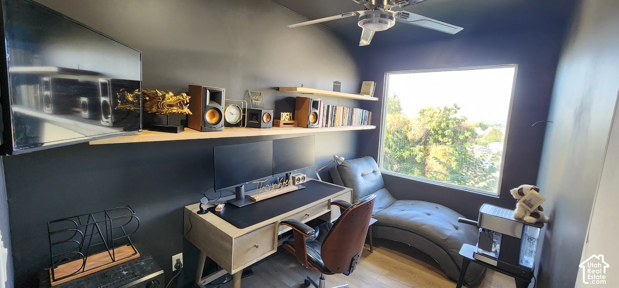 Wood-finish flooring, ceiling fan with integrated lighting, built-in shelving, large window, and dark painted walls