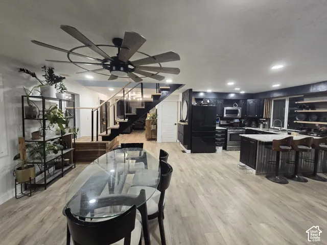 Open-concept living space featuring wood-finish flooring throughout, a black kitchen with stainless steel appliances and island seating, recessed lighting, and a ceiling fan