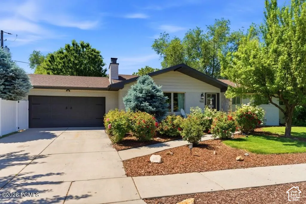 Single-story residence featuring a two-car garage, concrete driveway, and a white fence