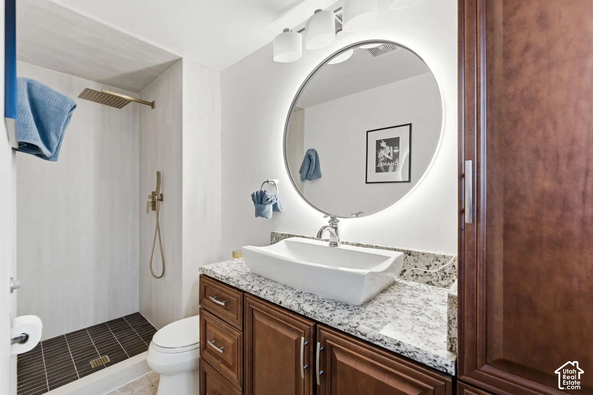 Shower with light-toned wall tile and dark floor tile, featuring a rain showerhead and hand shower
