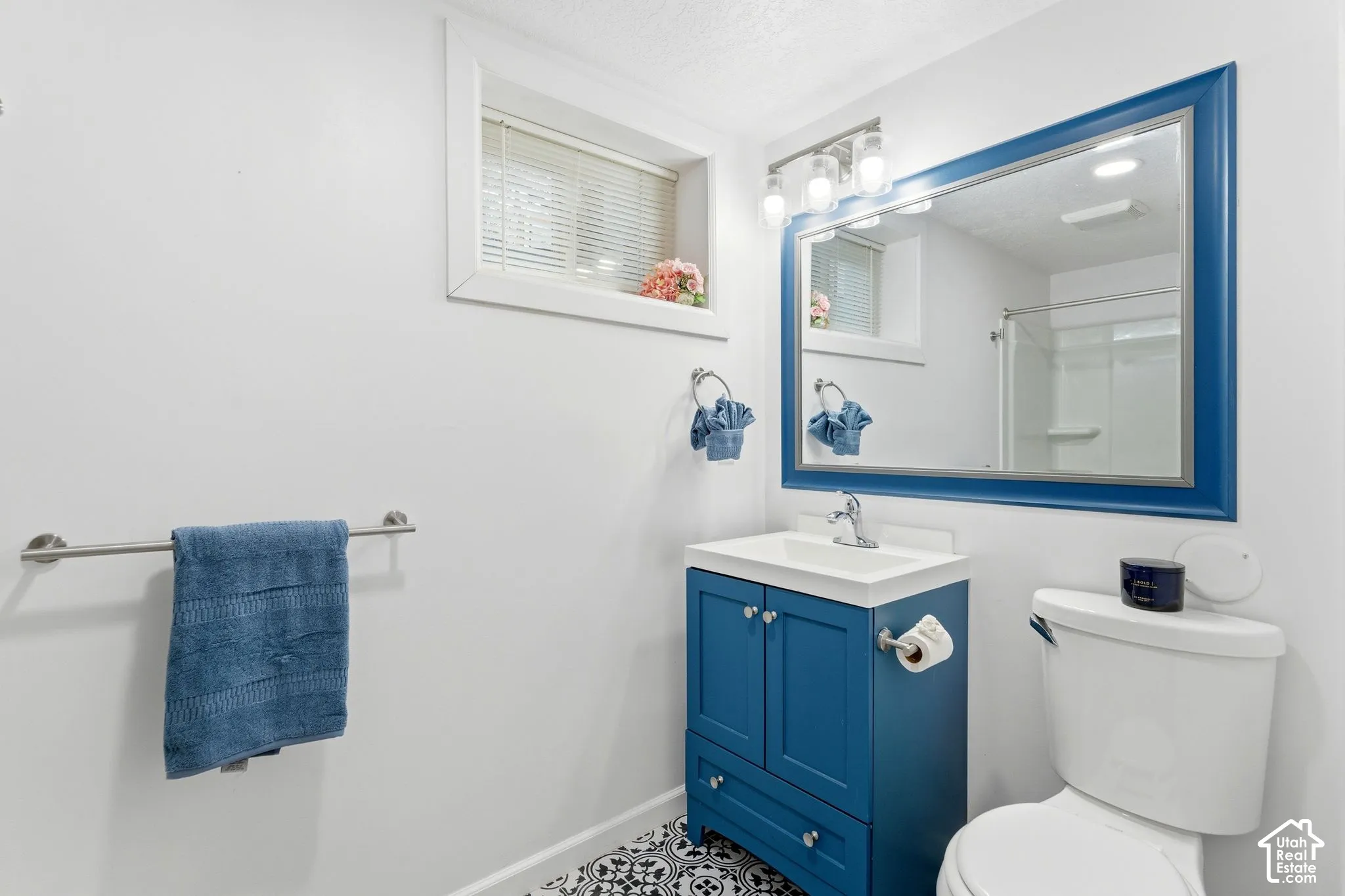 Modern bathroom featuring a blue vanity with a white countertop sink, a framed mirror, and patterned floor tiling