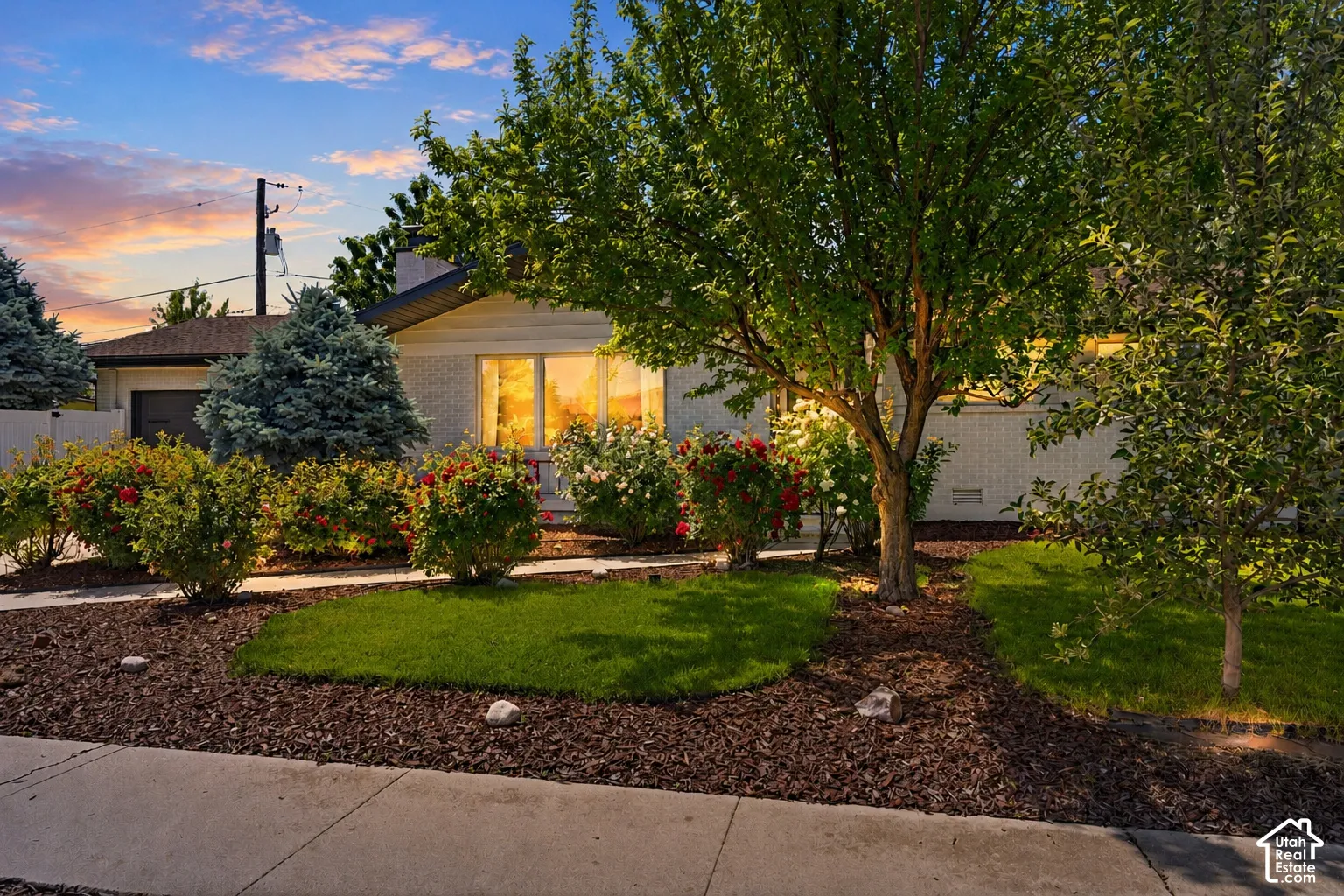 Manicured front yard with mature trees and established shrubbery, featuring a concrete walkway and a brick exterior