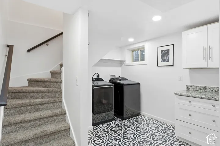 Laundry area featuring patterned floor tiles, white cabinetry with silver hardware, and a speckled countertop