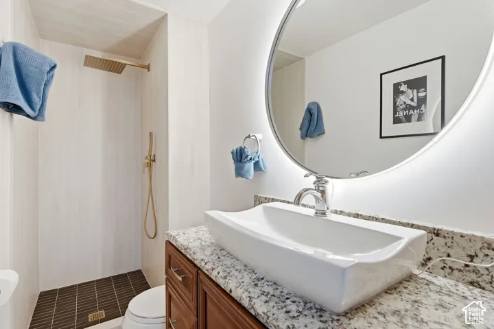 Recessed shower with gold-tone fixtures, vessel sink, granite-style countertop, dark wood-finish vanity, and illuminated round mirror