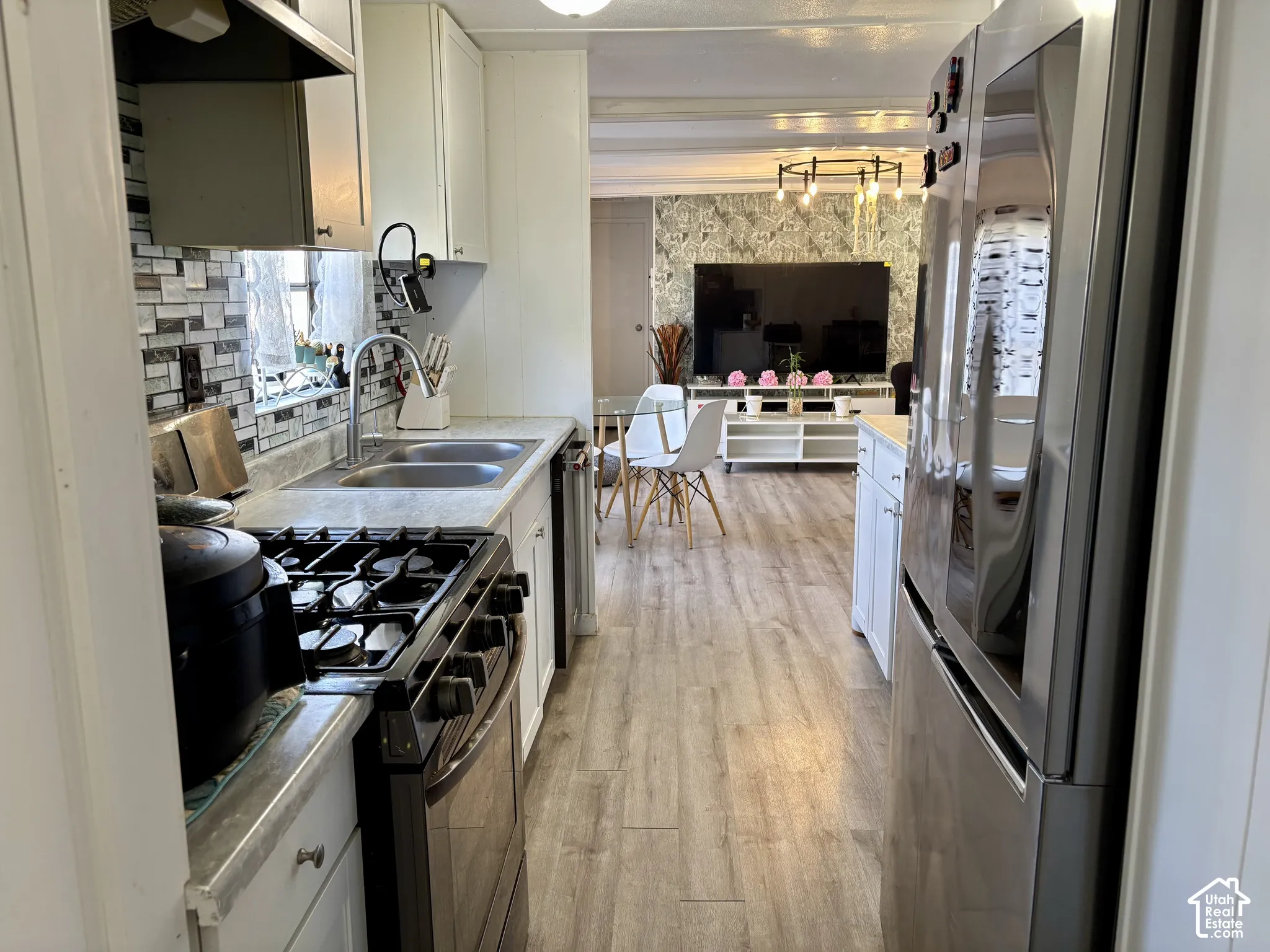 Galley kitchen featuring a gas range, dual-basin stainless steel sink, tile backsplash, and light wood-finish flooring