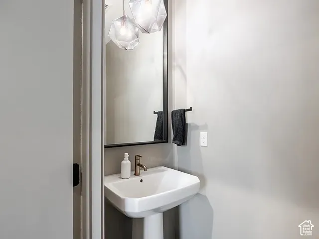 Pedestal sink with a wall-mounted mirror, geometric pendant lighting, and a modern bronze-finish faucet