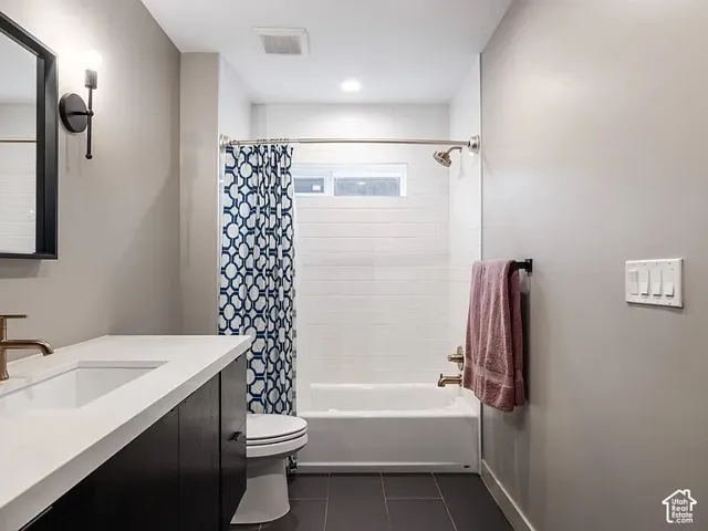 Bathroom featuring a single vanity with integrated sink, dark wood-finish cabinetry, a tub-shower combination with white subway tile surround, and matte gray tile flooring
