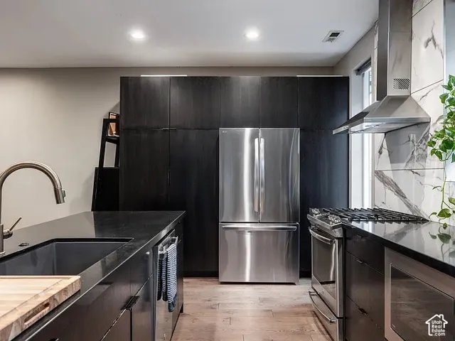Sleek kitchen with stainless steel appliances, dark cabinetry, wood-finish flooring, and a stone-finish backsplash