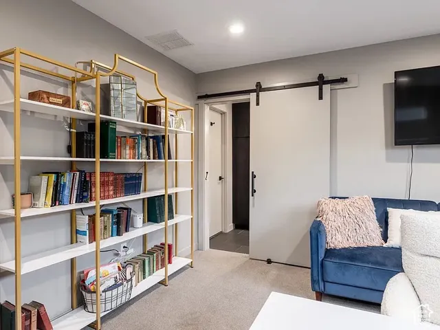 Custom built-in shelving with gold-finish framing, light gray walls, light gray carpeting, and a white sliding barn door