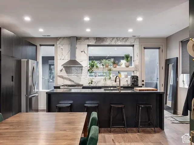 Gourmet kitchen featuring a large island, stainless steel appliances, wood-finish flooring, recessed lighting, and a full-height tile backsplash
