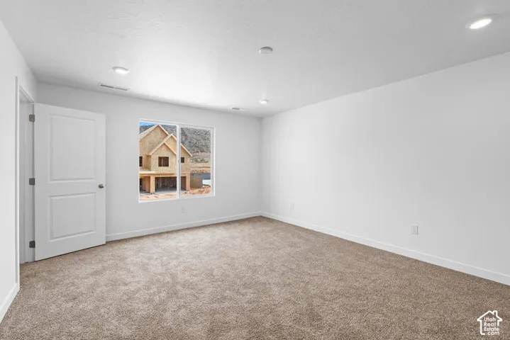 Neutral-toned carpet flooring, recessed ceiling lighting, a two-panel interior door, and a single window