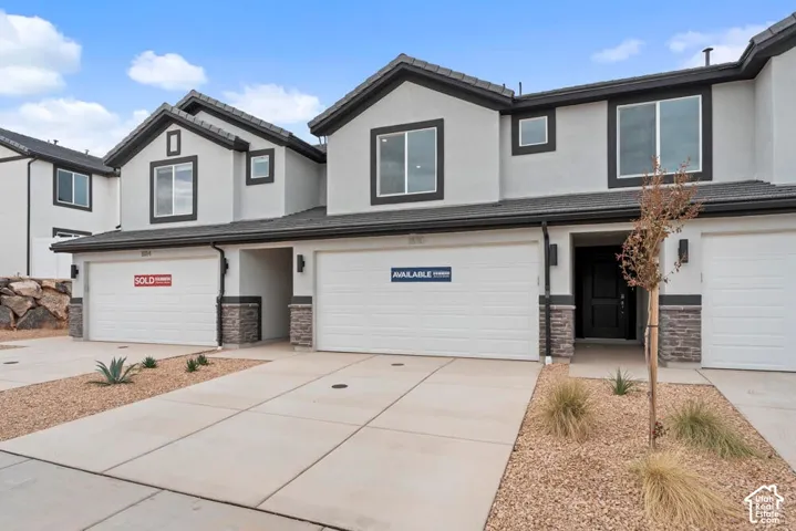 Contemporary exterior with light-colored stucco, dark trim, stone accents, two-car garage, and desert-style landscaping