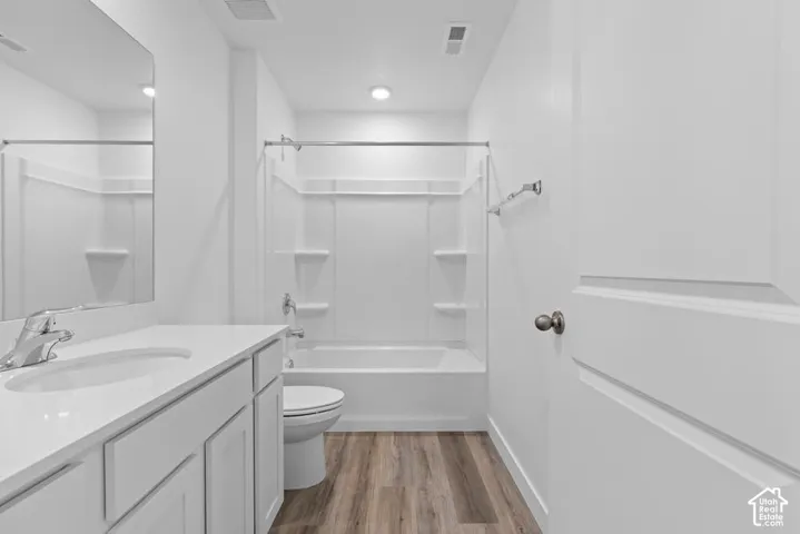 White vanity with an integrated sink, polished chrome faucet, wood-finish flooring, and a white shower/tub combination