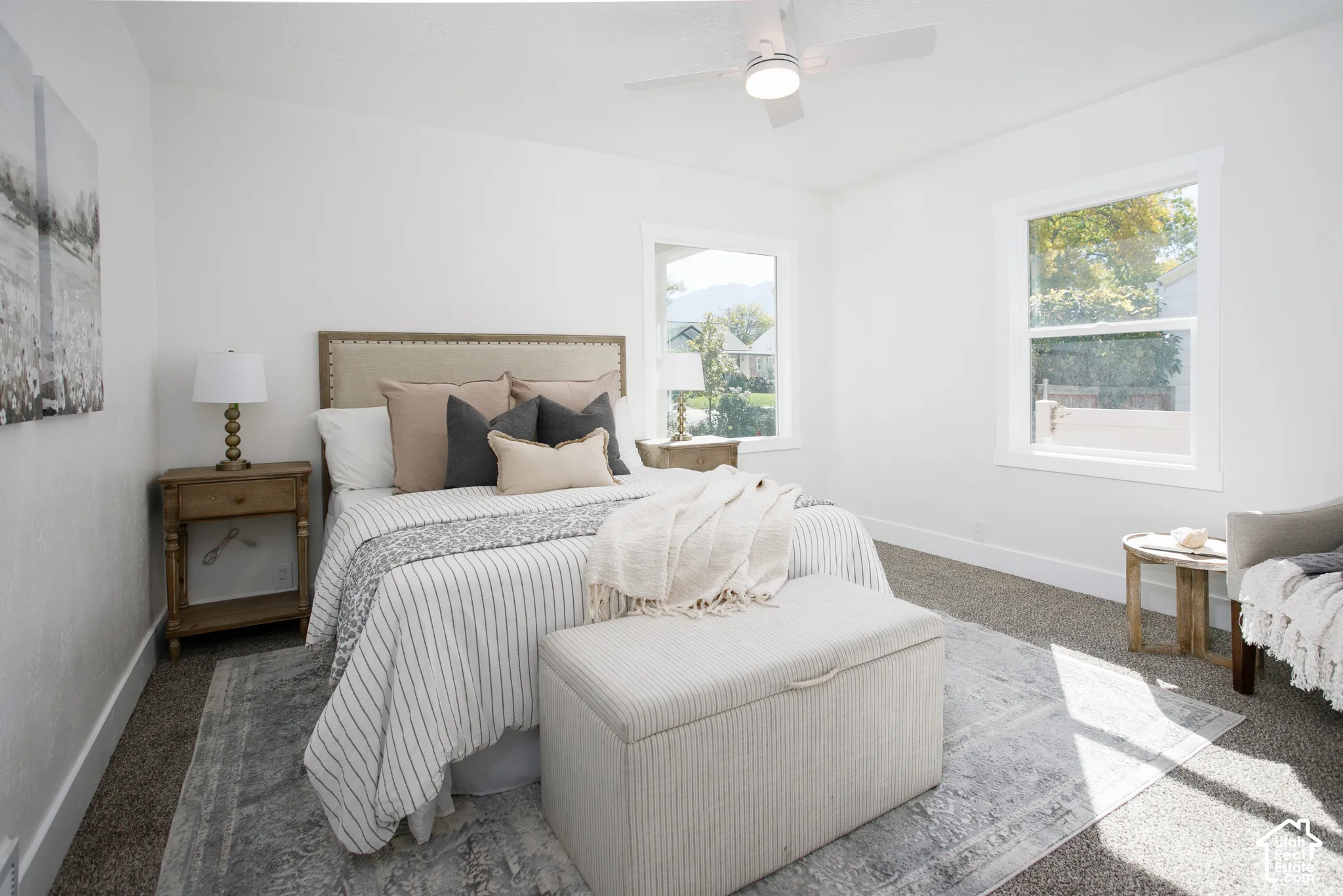 Bright interior with white walls, carpet flooring, a ceiling fan with integrated lighting, and two windows with white trim