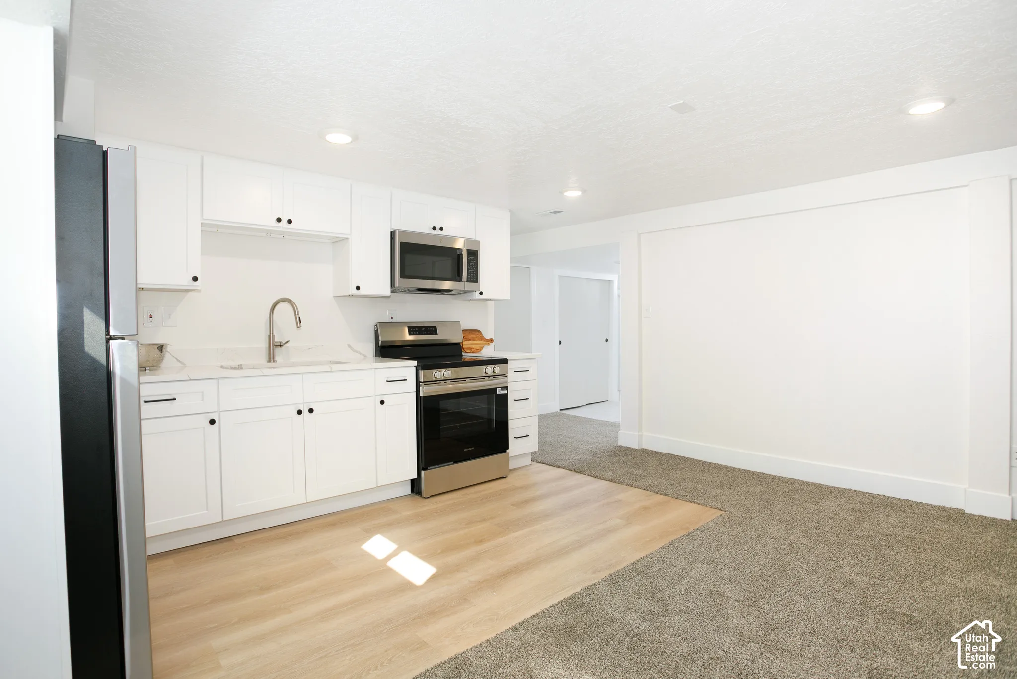 Modern kitchen featuring white cabinetry, stainless steel appliances, light-toned wood-finish flooring, and recessed lighting