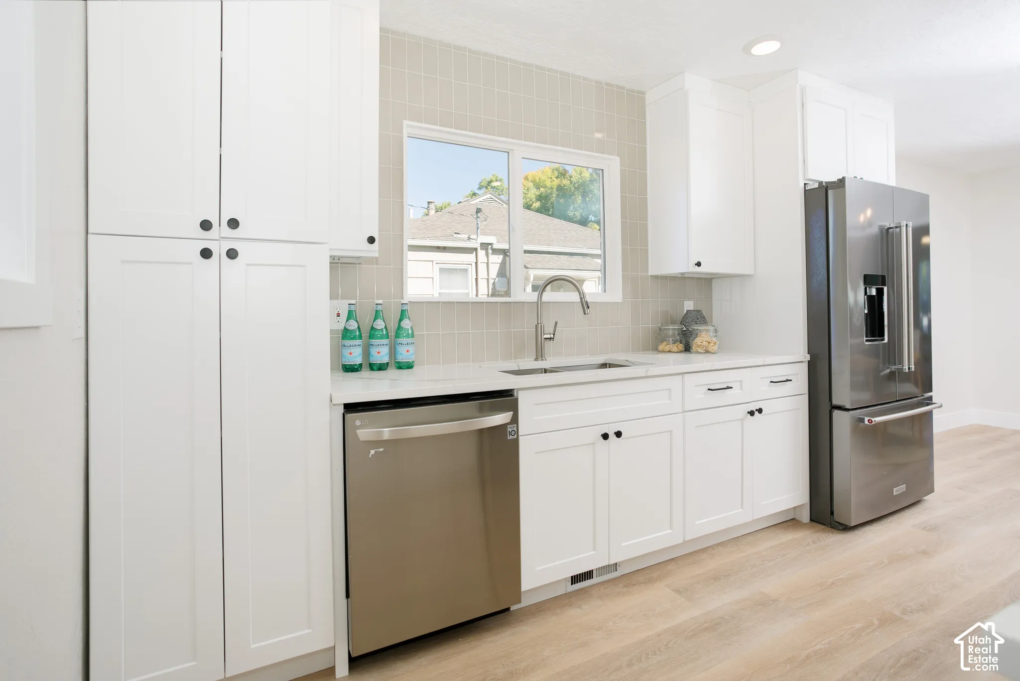 White cabinetry with matte black hardware, stainless steel appliances, light-toned wood-finish flooring, and subway tile backsplash
