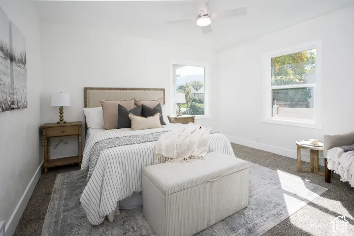 Bright interior with white walls, carpet flooring, a ceiling fan with integrated lighting, and two windows with white trim
