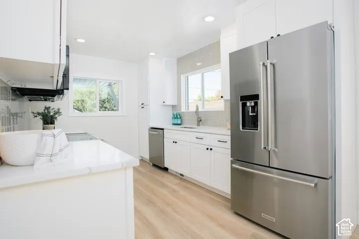 Kitchen featuring wood-finish flooring, recessed lighting, white cabinetry with black hardware, stainless steel appliances, and a tiled backsplash