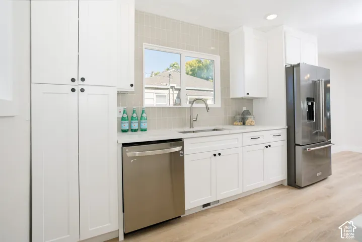 White cabinetry with matte black hardware, stainless steel appliances, light-toned wood-finish flooring, and subway tile backsplash