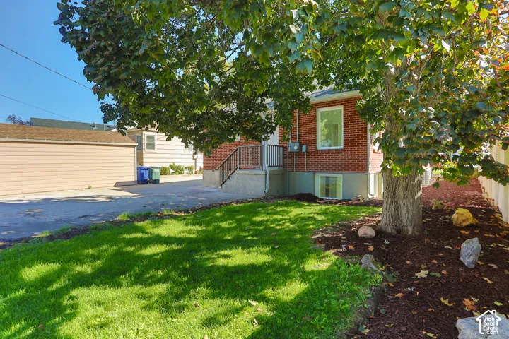 Brick exterior, rear-entry staircase with metal railing, lawn area, mulched planting beds, mature tree