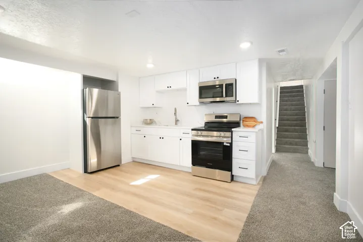Modern kitchen featuring white cabinetry with black hardware, stainless steel appliances including a gas range and built-in microwave, wood-finish flooring, and recessed ceiling lighting