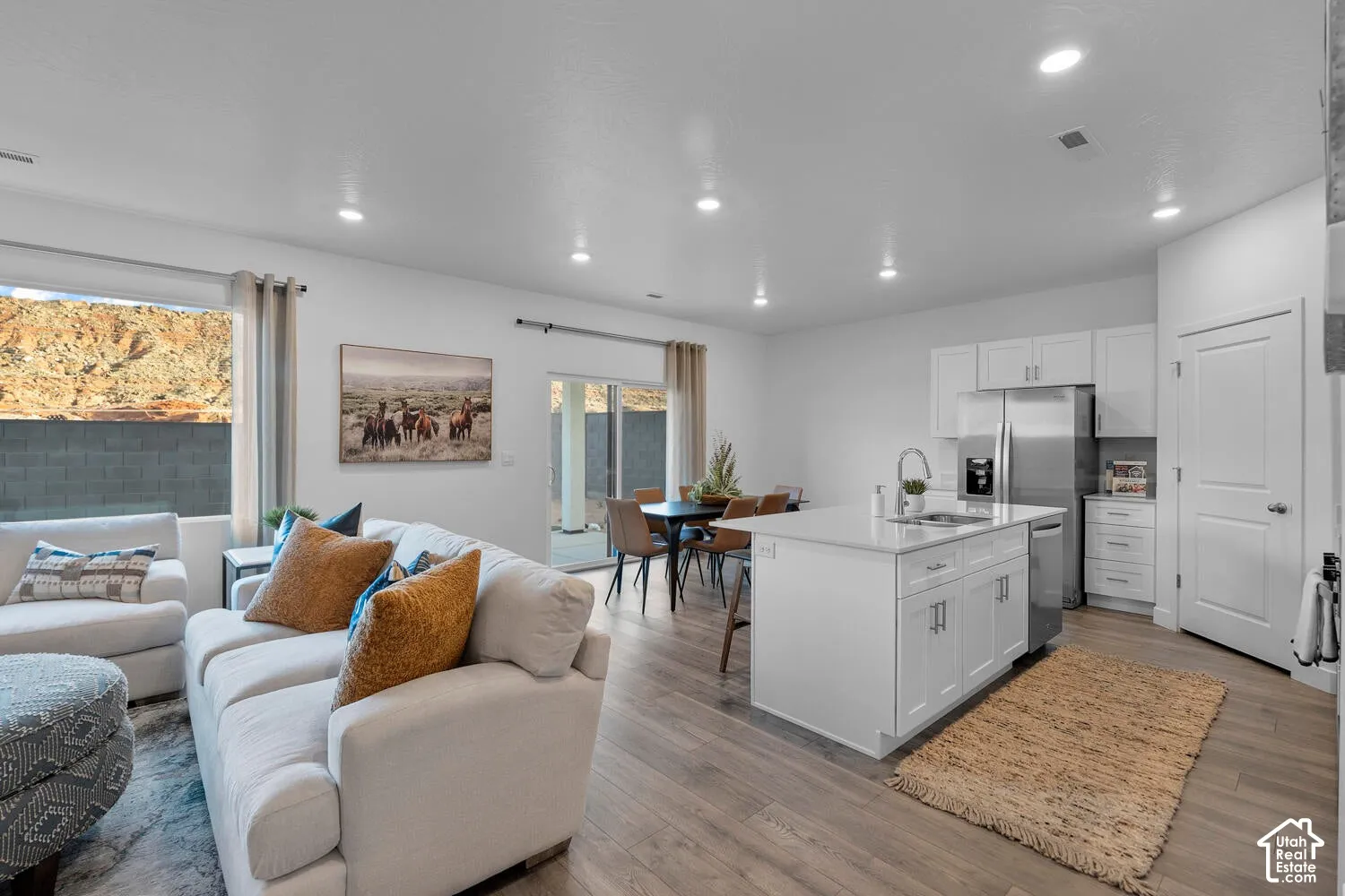 Open-concept living area featuring wood-finish flooring, recessed lighting, and a modern kitchen with a white island and stainless steel appliances