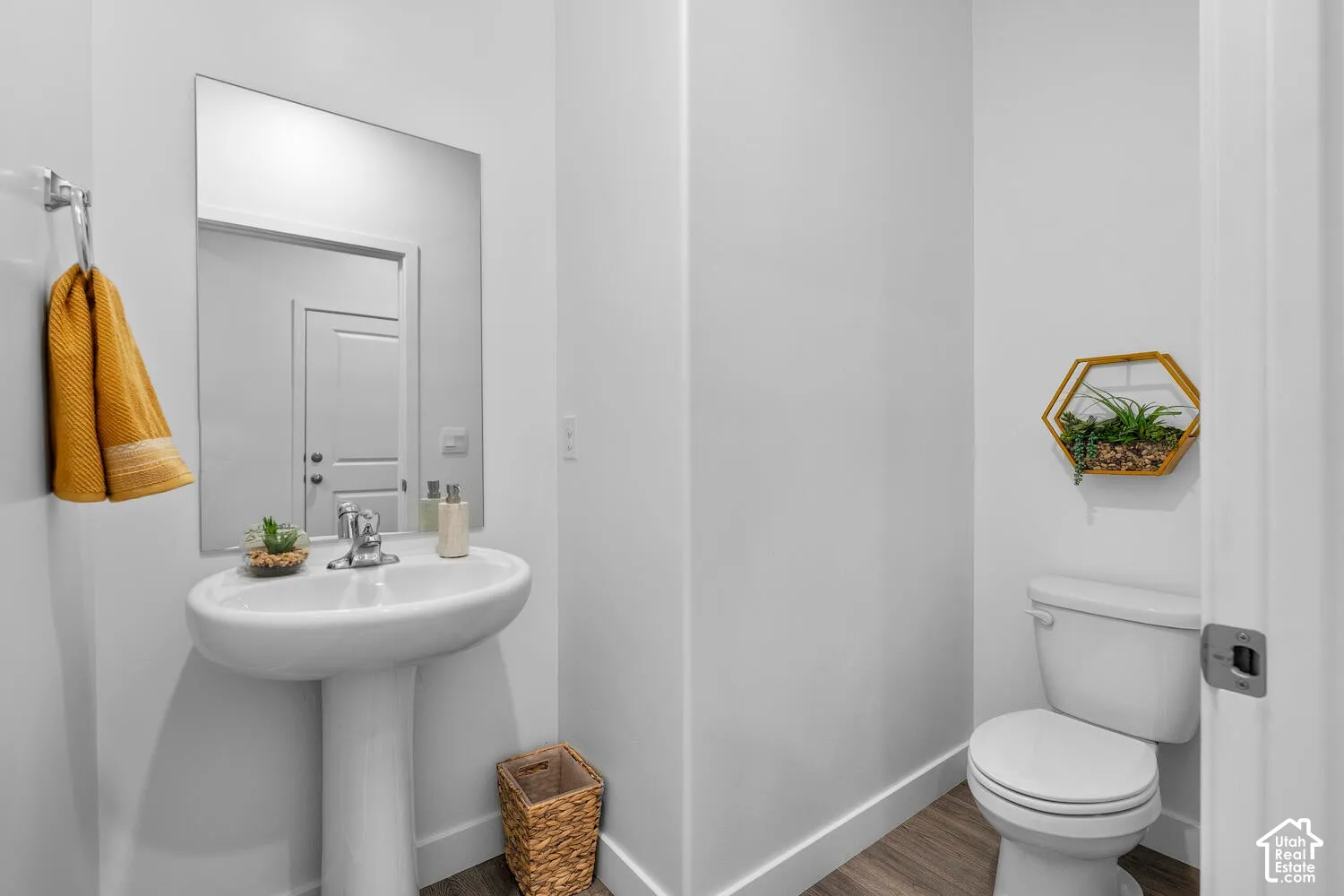 Pedestal sink with chrome faucet, large wall mirror, and wood-finish flooring