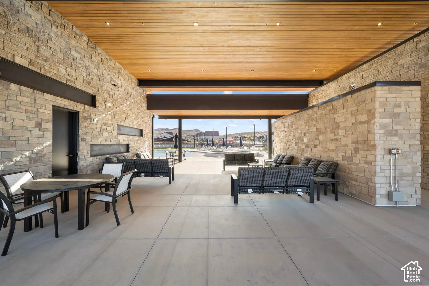 Covered outdoor lounge area featuring a wood-finish ceiling, stone accent walls, and concrete flooring