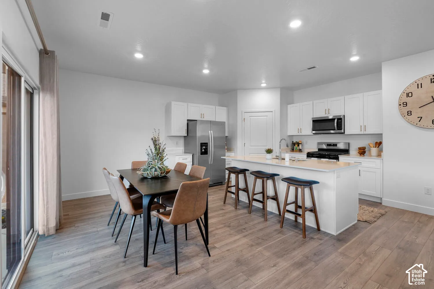 Open-concept living space with wood-finish flooring, white cabinetry, stainless steel appliances, a kitchen island with seating, and a sliding glass door