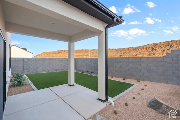 Covered patio with recessed lighting, artificial turf, gravel landscaping, and a concrete block perimeter wall