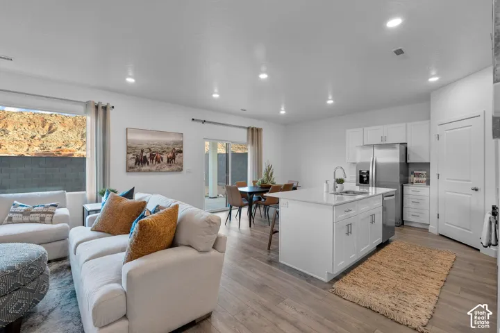 Open-concept living area featuring wood-finish flooring, recessed lighting, and a modern kitchen with a white island and stainless steel appliances