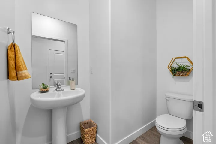 Pedestal sink with chrome faucet, large wall mirror, and wood-finish flooring