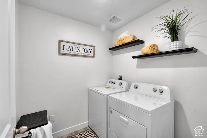 Dedicated laundry area featuring a white washer and dryer set, two wall-mounted floating shelves, and wood-finish flooring