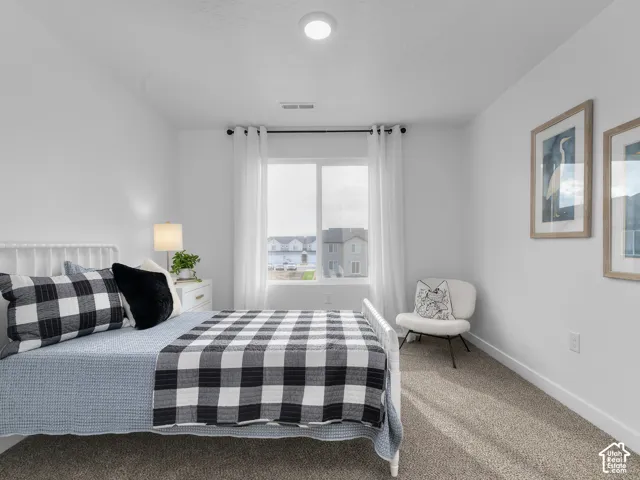 Bright bedroom with textured carpet flooring, a window offering natural light, and a built-in overhead light fixture