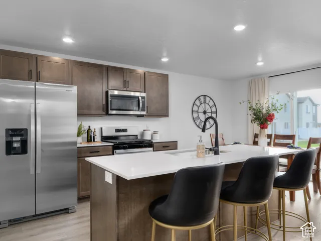 Kitchen featuring stainless steel appliances, dark wood-finish cabinetry, a large kitchen island with a sink, and recessed lighting