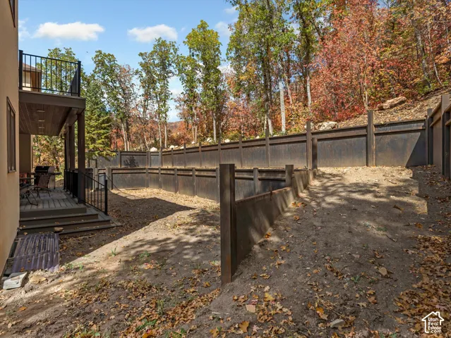Tiered backyard featuring multi-level retaining walls, expansive wooden deck with black metal railing, and dense mature timber backdrop
